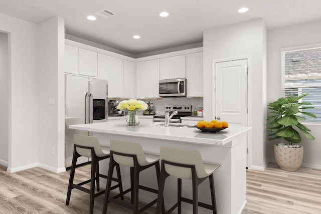 kitchen featuring appliances with stainless steel finishes, a kitchen island with sink, light stone counters, tasteful backsplash, and white cabinets