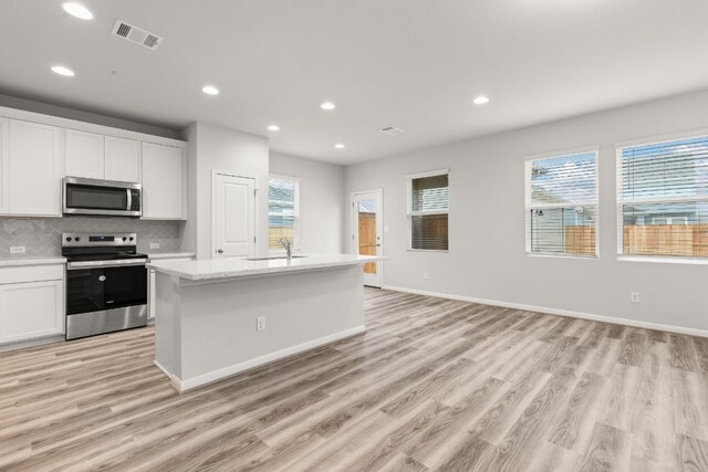 kitchen with light hardwood / wood-style flooring, appliances with stainless steel finishes, tasteful backsplash, white cabinets, and a center island with sink