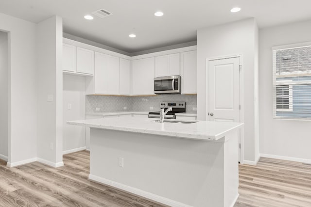 kitchen with sink, stainless steel appliances, light stone countertops, white cabinets, and a center island with sink