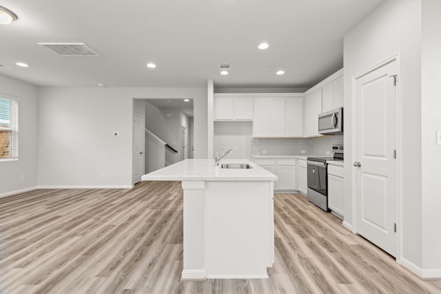 kitchen with sink, backsplash, stainless steel appliances, white cabinets, and a center island with sink