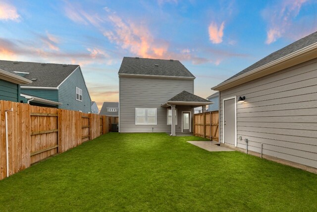 back house at dusk with central AC and a lawn