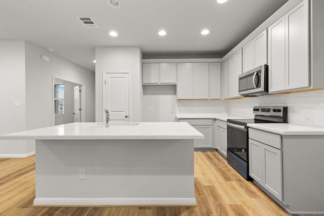 kitchen featuring range with electric stovetop, an island with sink, sink, and light hardwood / wood-style floors