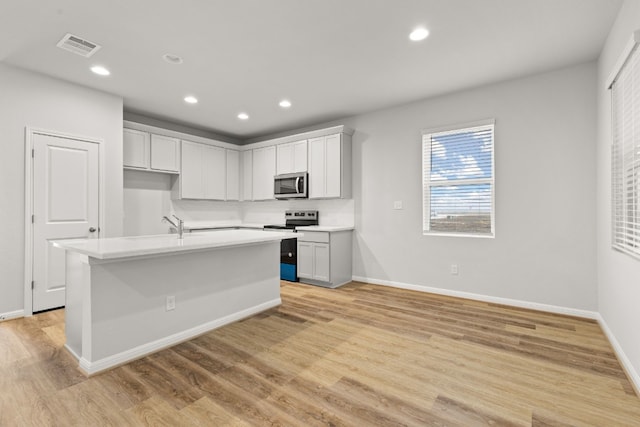 kitchen with appliances with stainless steel finishes, a kitchen island with sink, and light hardwood / wood-style floors