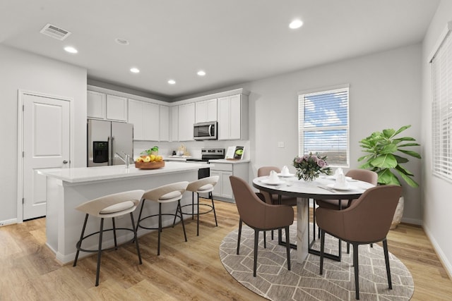 kitchen featuring white cabinetry, light hardwood / wood-style floors, stainless steel appliances, and an island with sink