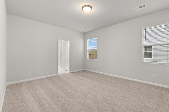 empty room with light colored carpet and a textured ceiling