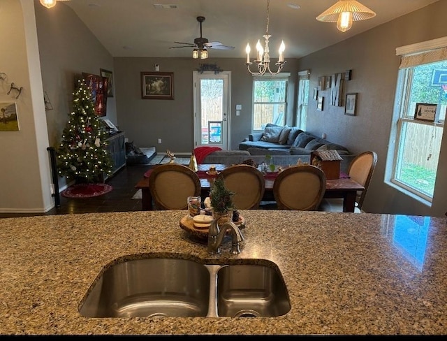 kitchen featuring sink, light stone counters, lofted ceiling, decorative light fixtures, and ceiling fan with notable chandelier