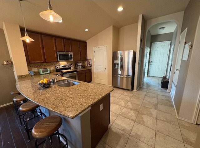 kitchen featuring light stone countertops, sink, stainless steel appliances, pendant lighting, and a breakfast bar