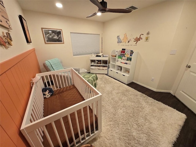 bedroom with a crib, dark hardwood / wood-style flooring, and ceiling fan