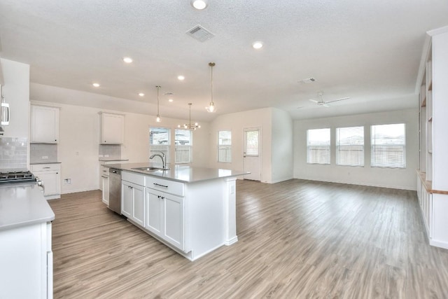 kitchen with white cabinetry, sink, stainless steel dishwasher, pendant lighting, and a center island with sink