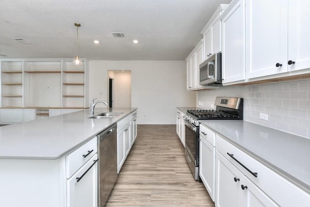 kitchen featuring stainless steel appliances, a kitchen island with sink, sink, white cabinets, and hanging light fixtures