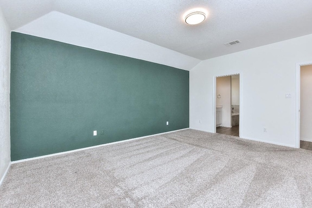 unfurnished bedroom featuring a textured ceiling, connected bathroom, carpet flooring, and lofted ceiling