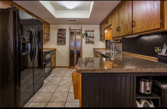 kitchen with a tray ceiling, sink, light tile patterned floors, kitchen peninsula, and black fridge