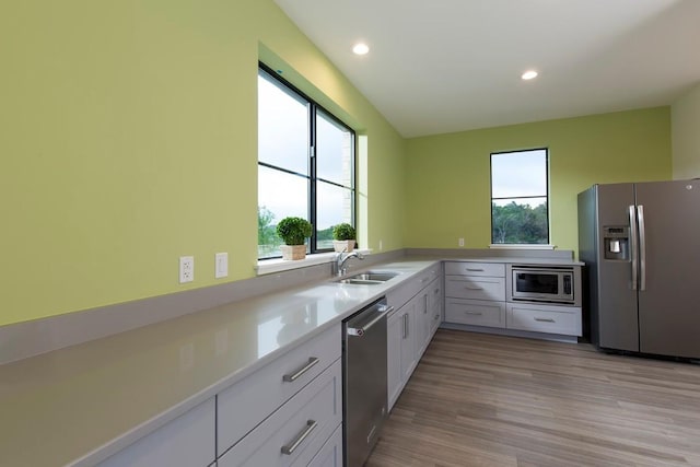 kitchen featuring light wood finished floors, stainless steel appliances, light countertops, a sink, and recessed lighting