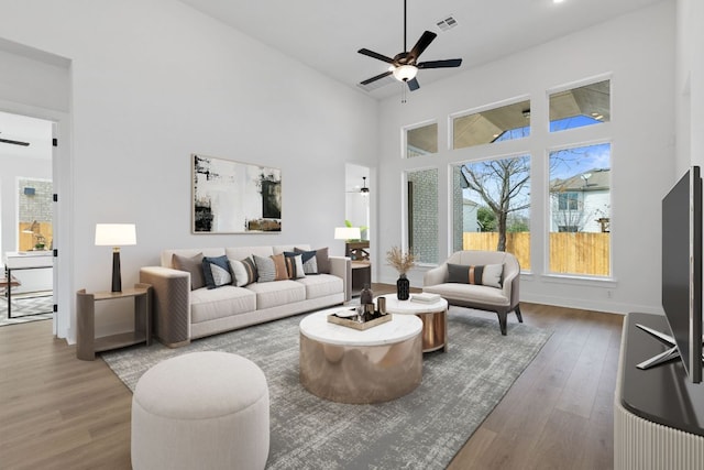 living area featuring baseboards, visible vents, a ceiling fan, a towering ceiling, and wood finished floors