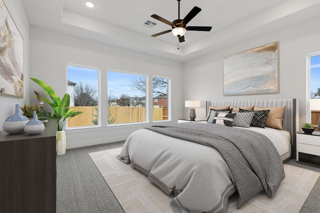 bedroom featuring a tray ceiling, visible vents, light carpet, and baseboards