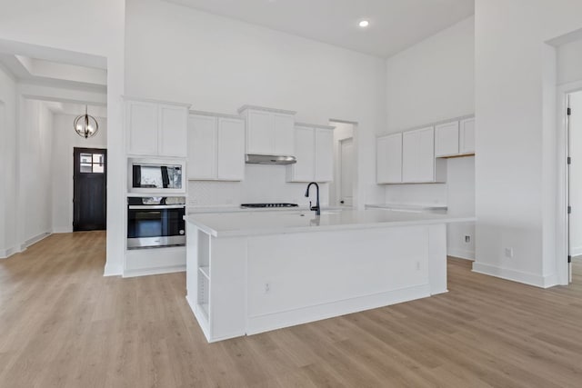 kitchen featuring oven, a high ceiling, built in microwave, under cabinet range hood, and white cabinetry