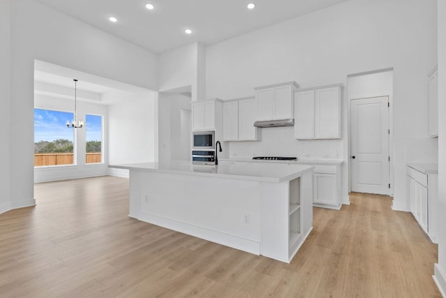 kitchen with stainless steel appliances, light countertops, an inviting chandelier, light wood-style floors, and under cabinet range hood