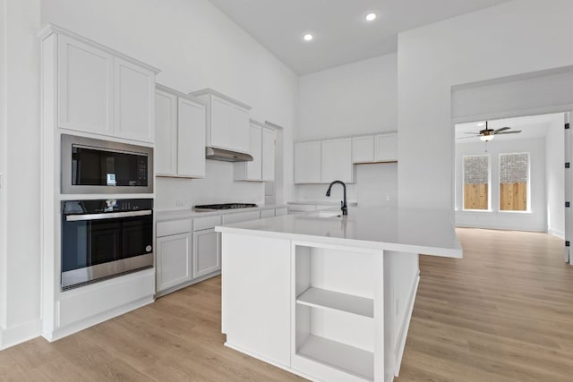 kitchen featuring a towering ceiling, built in microwave, under cabinet range hood, stainless steel oven, and a sink