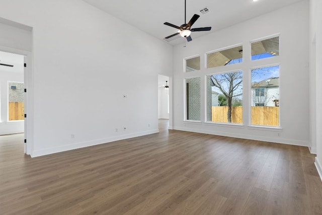 unfurnished living room with wood finished floors, visible vents, a towering ceiling, a ceiling fan, and baseboards