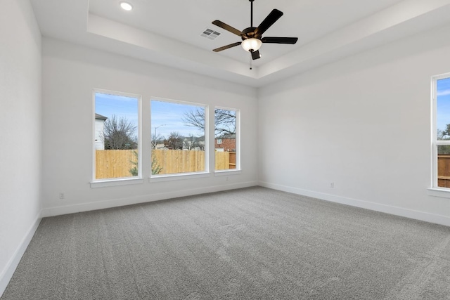 carpeted empty room with a tray ceiling, a ceiling fan, visible vents, and baseboards