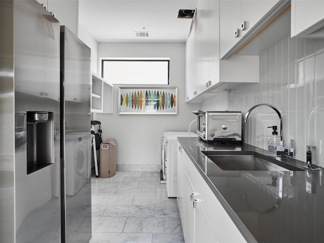 kitchen featuring backsplash, sink, white cabinets, and washer and dryer