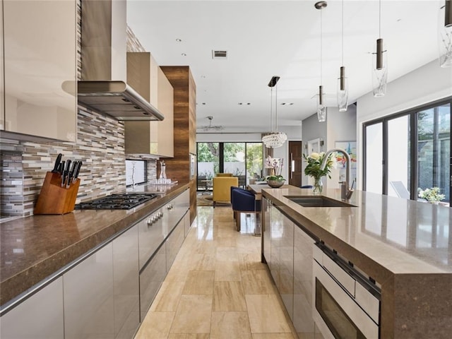 kitchen featuring sink, decorative light fixtures, wall chimney exhaust hood, decorative backsplash, and a notable chandelier