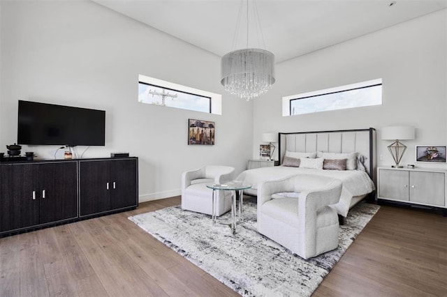 bedroom featuring hardwood / wood-style floors, a towering ceiling, and an inviting chandelier