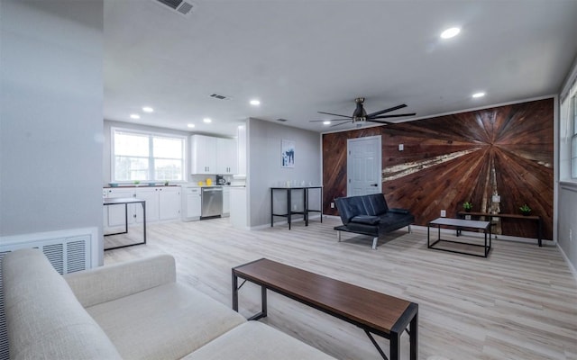 living room with a barn door, wood walls, ceiling fan, and light wood-type flooring