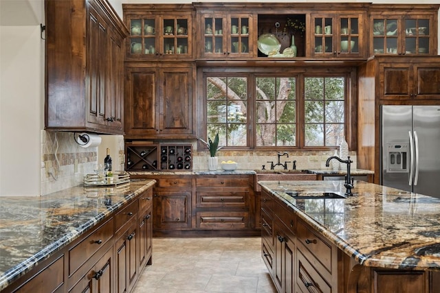 kitchen with sink, stainless steel refrigerator with ice dispenser, stone counters, and tasteful backsplash