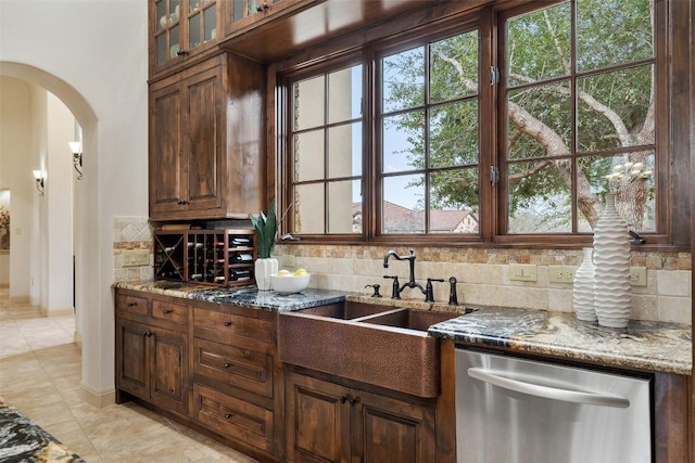 kitchen with decorative backsplash, stone countertops, stainless steel dishwasher, and sink