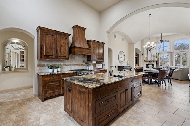 kitchen with custom exhaust hood, a center island with sink, sink, decorative light fixtures, and light stone counters