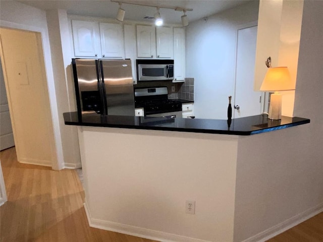 kitchen featuring stainless steel appliances, kitchen peninsula, track lighting, decorative backsplash, and white cabinets