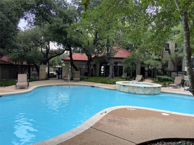 view of swimming pool with pool water feature and a hot tub