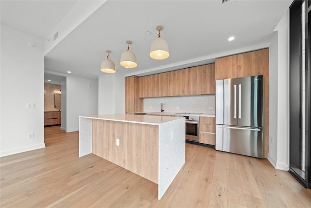 kitchen featuring appliances with stainless steel finishes, backsplash, sink, decorative light fixtures, and light hardwood / wood-style flooring