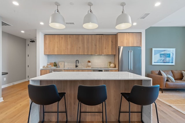 kitchen featuring pendant lighting, sink, stainless steel fridge, tasteful backsplash, and light hardwood / wood-style floors