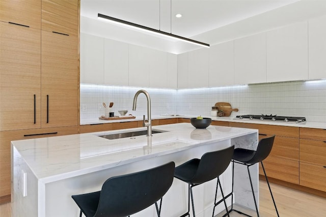 kitchen with white cabinets, tasteful backsplash, a kitchen island with sink, and sink