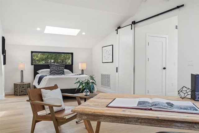 bedroom featuring vaulted ceiling with skylight, a barn door, and light hardwood / wood-style floors