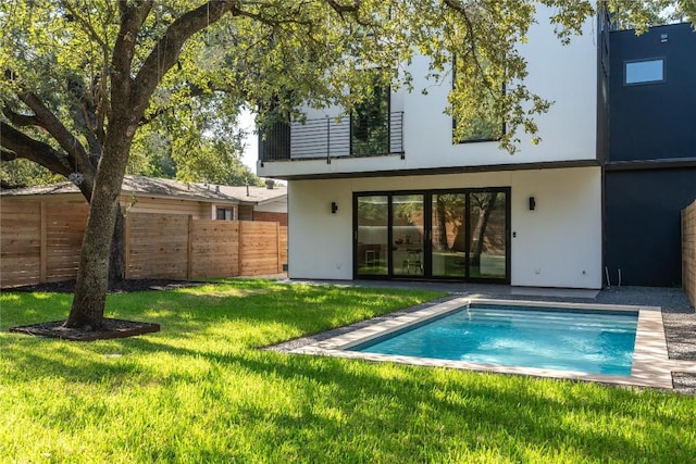 rear view of house with a fenced in pool, a balcony, and a yard