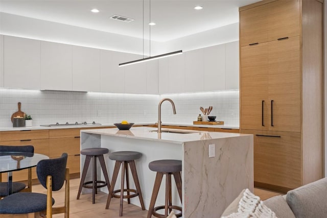 kitchen with backsplash, a kitchen island with sink, a kitchen breakfast bar, gas stovetop, and white cabinetry