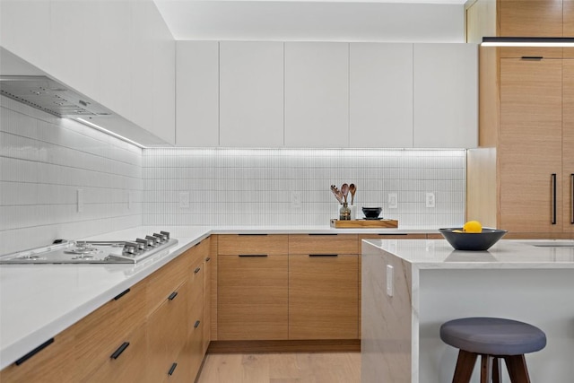 kitchen featuring backsplash, a breakfast bar, white gas cooktop, light hardwood / wood-style flooring, and white cabinets