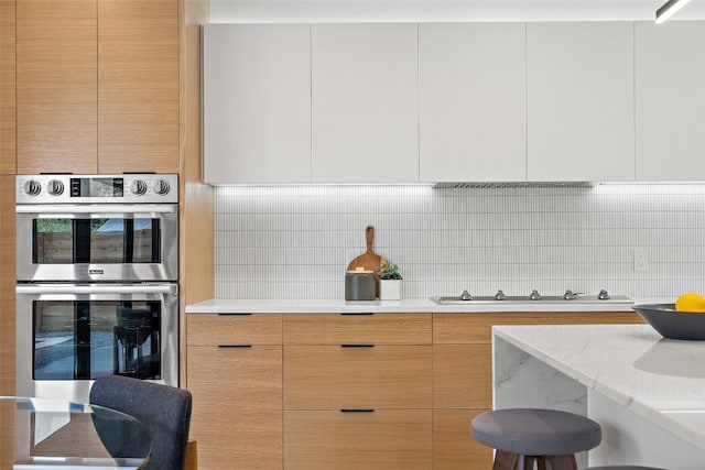 kitchen featuring stainless steel double oven, light stone counters, white gas cooktop, backsplash, and white cabinets