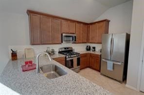 kitchen with sink, light stone counters, kitchen peninsula, vaulted ceiling, and appliances with stainless steel finishes