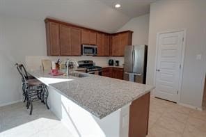 kitchen with kitchen peninsula, appliances with stainless steel finishes, a kitchen breakfast bar, vaulted ceiling, and sink