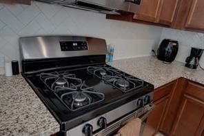 kitchen with black gas range, light stone countertops, and tasteful backsplash