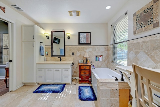 bathroom with tile patterned floors, vanity, a relaxing tiled tub, and tile walls