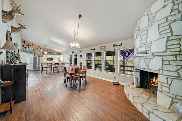 dining space with hardwood / wood-style floors, an inviting chandelier, a stone fireplace, and vaulted ceiling