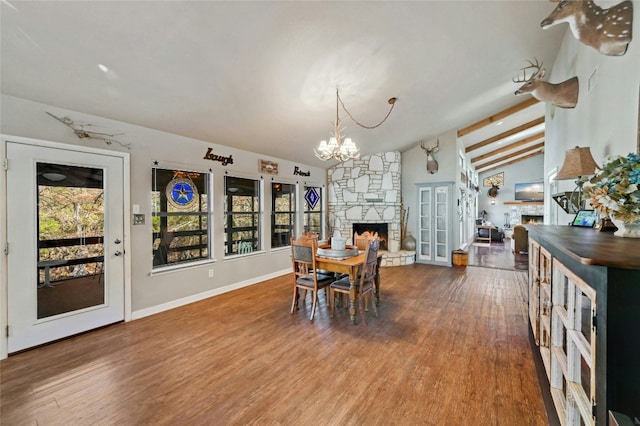 dining space with hardwood / wood-style floors, lofted ceiling with beams, and a stone fireplace