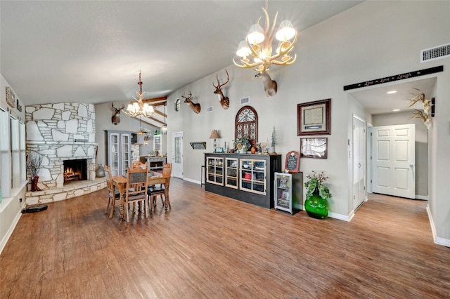 dining area featuring a stone fireplace, hardwood / wood-style flooring, lofted ceiling, and a notable chandelier