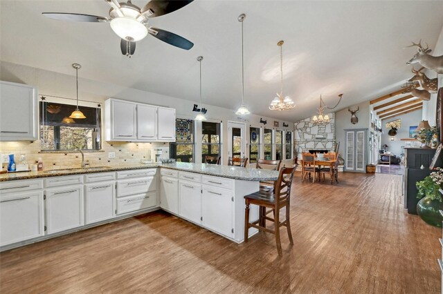 187 N Roy Chisum Rd, Leakey, TX 78873 - kitchen with vaulted ceiling, a chandelier, backsplash, wood finished floors, and white cabinetry
