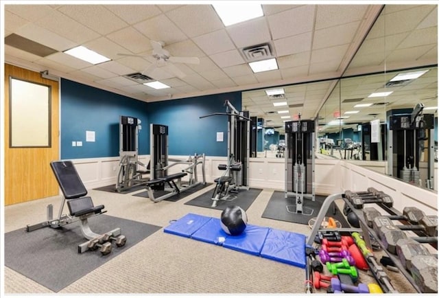 gym featuring carpet flooring, a paneled ceiling, ceiling fan, and wood walls